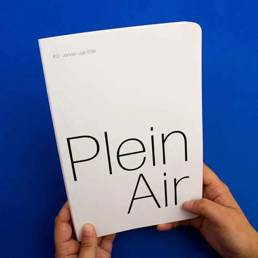 Livre tenu fermé, de face, la couverture est blanche avec les mots "Plein Air" écrit en grand et finement.